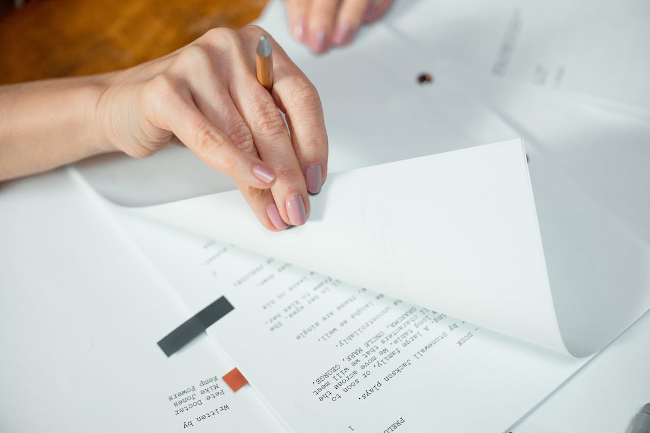 Close-up image of hands turning pages of a document on a desk indoors.