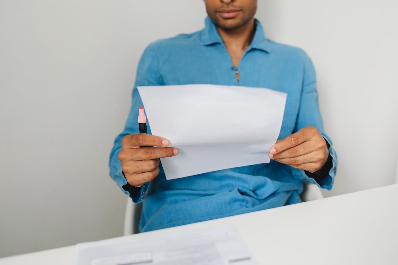 Close-up of a man holding and examining a paper with a pen indoors.